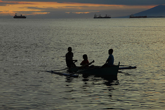 Three boys paddling a small outrigger boat just off Paradise Island Beach on Samal Island.