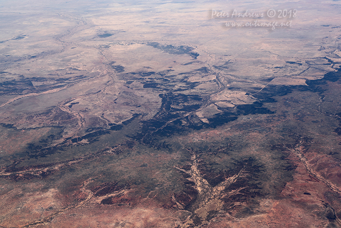 Fence-lines and dirt tracks scar the landscape. Looking towards the northeast edge of the Channel Country where any water from flodding storms flows towards central South Australia, Outback Queensland. 21°11'52.1"S 144°27'32.7"E. High altitude shots from a flight between Sydney Australia and Manila, Philippines.