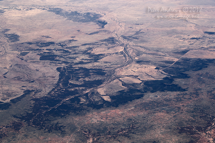 Fence-lines and dirt tracks scar the landscape. Looking towards the northeast edge of the Channel Country where any water from flodding storms flows towards central South Australia, Outback Queensland. 21°11'52.1"S 144°27'32.7"E. High altitude shots from a flight between Sydney Australia and Manila, Philippines.