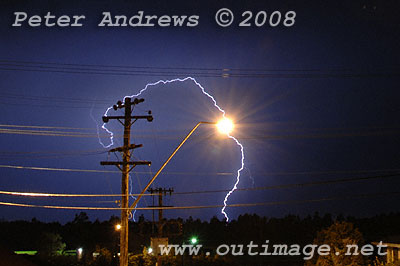 Lightning behind a power pole appears to pass through a street light.