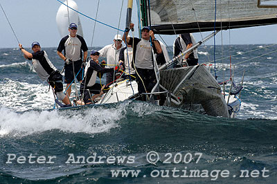 Looking towards the front of Lang Walker's Farr 40 Kokomo under spinnaker ploughing through the ocean, much of the boat in hidden behind a wave